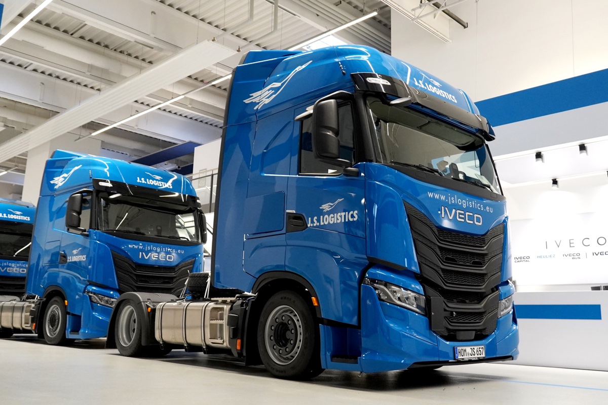 Два синих грузовика IVECO с брендингом J.S. Logistics стоят в светлом помещении логистического центра.